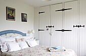 Blue headboard on quilted bed in bedroom with white painted and hinged built-in wardrobes, Oxfordshire, England, UK