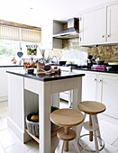 Wooden stools at kitchen island in kitchen of barn conversion in Oxfordshire, England, UK
