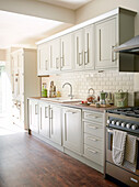 Light green fitted kitchen with cream tiled splashback and wooden floor in North London home, England, UK