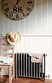 Sunhat on back of chair next to radiator below large clock with roman numerals, North London home, England, UK