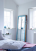 Aus einem alten Fenster wurde ein Spiegel in der Ecke eines weißen Schlafzimmers in einem Landhaus in Devonshire, Großbritannien