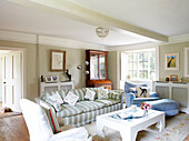 Striped sofa and armchair with footstool in living room of Oxfordshire farmhouse England UK