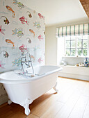 Freistehende Badewanne mit Rolltop und Tapete in einem Badezimmer in Oxfordshire, England UK