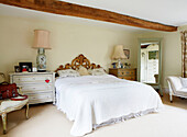 Double bed with gilt headboard in beamed Oxfordshire farmhouse bedroom England UK