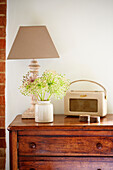 Vintage radio and cut flowers with lamp on wooden chest of drawers in Surrey farmhouse England UK