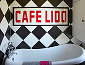 Sign reading 'CAFE LIDO' on chequered wall above freestanding bath in Margate family home Kent England UK