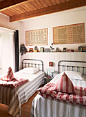 Twin beds with striped linen below shelf with toys and artwork in schoolhouse conversion Brittany France