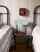 Vintage chair and book between metal headboards in twin bedroom of schoolhouse conversion Brittany France