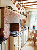 Copper saucepans hang above Aga in exposed brick fireplace of Derbyshire farmhouse kitchen England UK