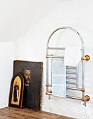 Wall-mounted chrome radiator and vintage artwork in attic bathroom of traditional country house Welsh borders UK