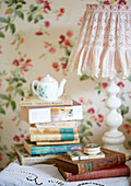 Lampenschirm aus Spitze mit einem Stapel Bücher und einer Teekanne auf einem Nachttisch in einem Landhaus in Oxfordshire, England, UK