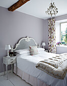 Lilac bedroom with classic headboard and folded quilt in rural Oxfordshire cottage England UK