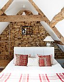 Beamed attic bedroom with exposed stone wall in rural Oxfordshire cottage England UK