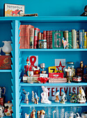Books on parrot figurines with vintage toys on bright blue shelving in Auckland home North Island New Zealand