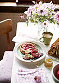 Marmelade und Brot mit Schnittblumen auf dem Frühstückstisch in einem bretonischen Landhaus in Frankreich