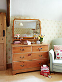 Wooden chest of drawers with light green armchair in bedroom of Devonshire cottage UK