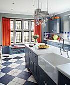 Bright orange curtains in grey fitted kitchen with butler sink in Northumbrian manor house England UK