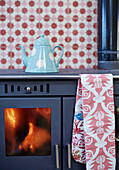 Spotted kettle on lit oven with patterned wallpaper and oven glove in Northumbrian home England UK