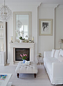 Cut tulips on buttoned ottoman with mirror on fireplace in white living room of York townhouse England UK