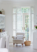 Striped armchair with basket in front of French doors with shutters in York townhouse England UK