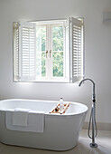 Freestanding bath below window with shutters in York townhouse England UK