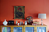 Lampe und Ornamente mit gerahmtem Porträt vor roter Wand in einem Haus in Speldhurst, Kent, England, UK