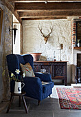 Blue wingback armchair with carved wooden sideboard in Grade II listed Tudor bastle Northumberland UK
