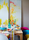 Cut tulips with grapefruit in bowls and modern artwork on dining table with cushions in studio,, UK