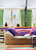 Dog on sofa with pink and purple cushions in front of window with green curtains in 18th century Northumbrian mill house, UK