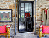 Novelty tiger benches on each side of black door in exposed stone wall 18th century Northumbrian mill house, UK