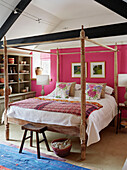 Carved wooden four poster and shelving unit in pink bedroom of 18th century Northumbrian mill house, UK