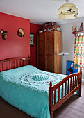 Turquoise bed cover on wooden bed with red feature wall in County Durham home, North East England, UK
