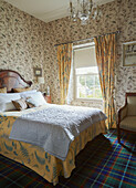 Double bed patterned wallpaper and tartan carpet in 19th century Georgian townhouse bedroom in Talgarth, Mid Wales, UK
