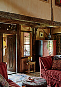 Red sofa with tapestry footstool and view through wooden doorway in Herefordshire farmhouse, UK