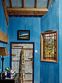 Stained glass window in blue room with fabric hanging on back of door in Herefordshire farmhouse, UK