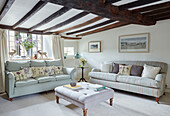 Light green sofas with buttoned ottoman in beamed living room of Oxfordshire cottage, UK