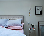 Pastel pillows with buttoned headboard and lightbulb above bedside table in Warwickshire farmhouse, England, UK
