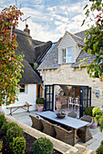 Wicker chairs at table in courtyard of renovated 17th century Cotswolds cottage, UK