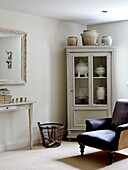 Corner cupboard with antique chinaware and upholstered armchair in West Sussex barn conversion, UK