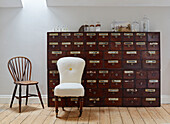 Vintage apothecary cabinet with upholstered chair in West Sussex barn conversion, UK