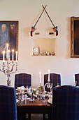 Beleuchtete Kerzen auf einem Esstisch mit Schottenkaro-Stühlen und Schwertern in einem schottischen Schloss, UK