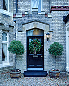 Christmas wreath on black front door of, UK home with planted trees