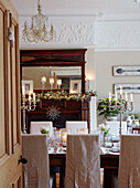 Slip-covered dining chairs with lit candles and carved antique mirror in, UK home