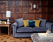 Yellow cushions on grey velvet Chesterfield in wood panelled living room of, UK home
