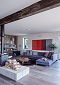 Woodburner with firewood and grey sofa in open plan living room Rye barn conversion, East Sussex