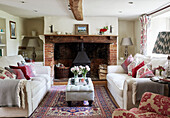 White sofas with red velvet cushions and exposed brick fireplace in Berkshire cottage, England, UK