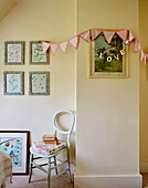 Botanical prints and bunting with chair and books in Sandford St Martin cottage, Oxfordshire, UK