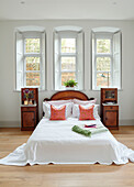 Low double bed with wooden cabinets below triple window in Woodstock home, Oxfordshire, UK