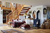 Red leather sofa and woodburner below open tread stairs in open plan Oxfordshire home, UK