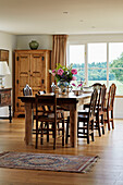 Cut flowers on wooden dining table with chairs in Oxfordshire farmhouse, UK